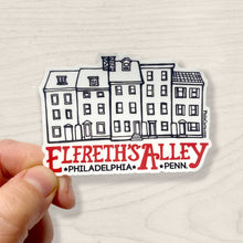 A hand holding a black and white sticker with 'Elfreth's Alley Philadelphia Penn.' text and a drawing of houses.